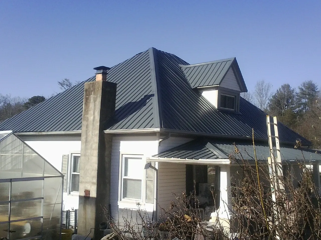 Dark blue standing seam metal roof on a white farmhouse with dormer — Slate & Tile Roof Repair by Roofing Brothers in Prole