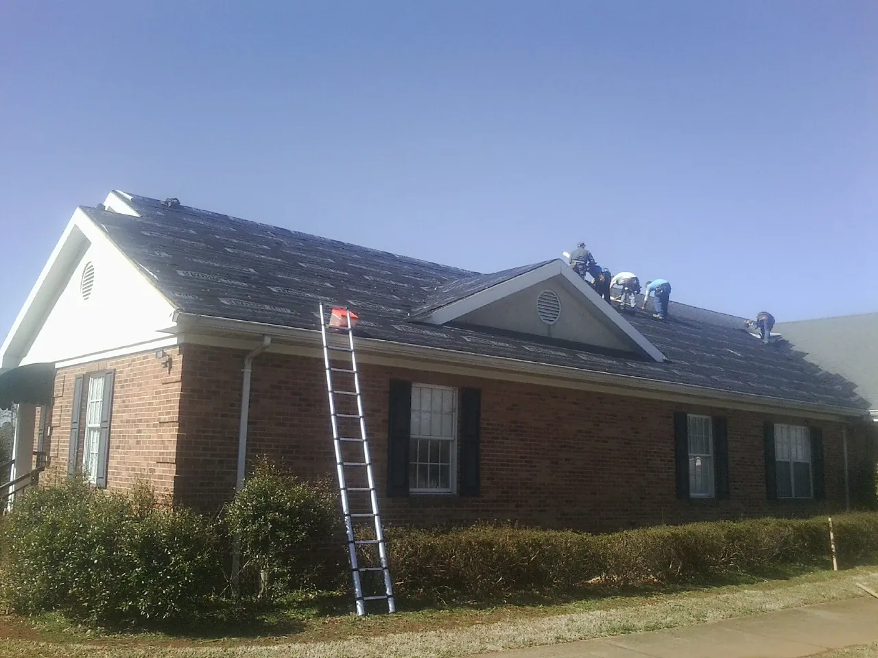 Crew tearing shingles off a brick ranch roof with a ladder set — Metal Roof Repair work by our crew in Prole