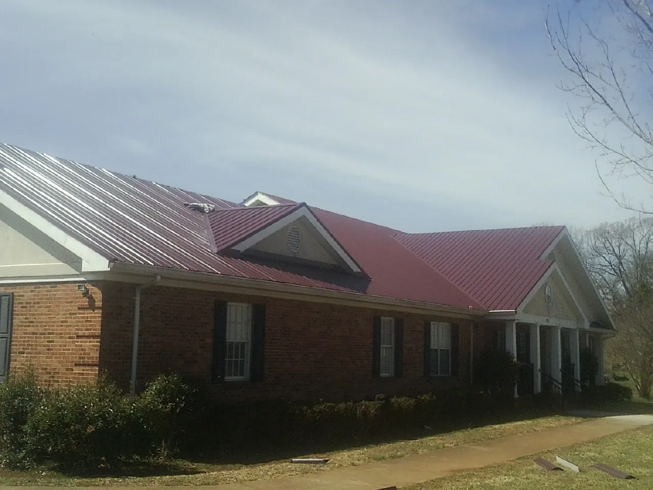 Red metal roof with gabled entries on a long brick building, from a Hail Damage Roof Repair job in Prole
