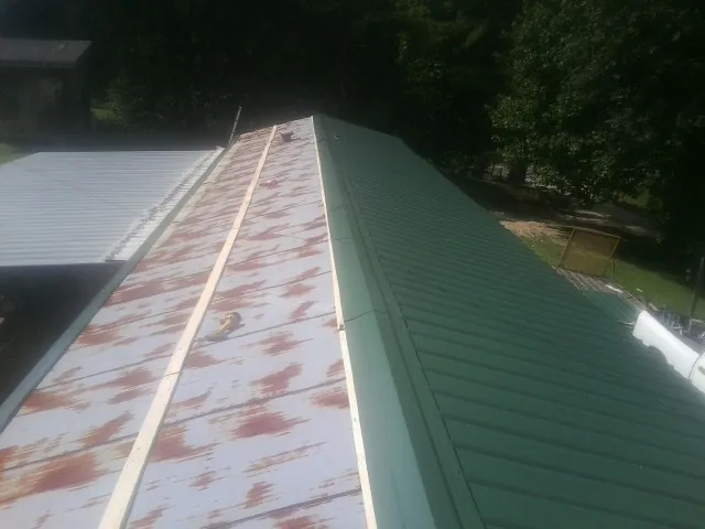 Old rusted panels beside newly installed green metal roofing — Wind Damage Roof Repair by Roofing Brothers in Prole