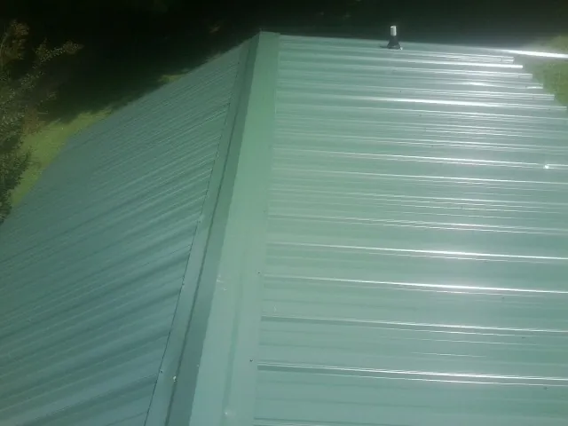New green metal panels meeting at the ridge of a roof — Flat Roof Repair work by our crew in Prole