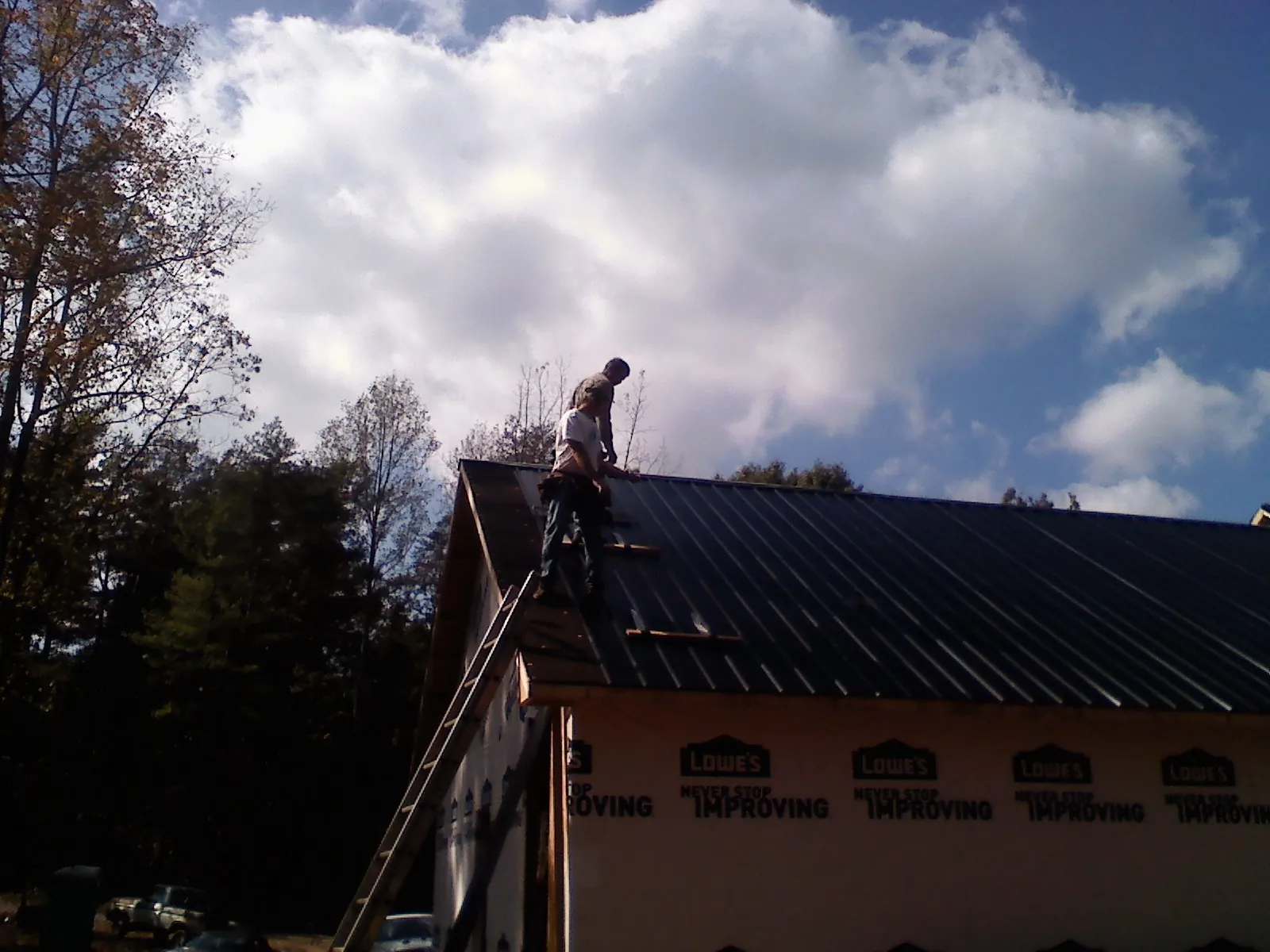 Roofer fastening dark metal panels high against a cloudy sky, from a Roof Inspection job in Prole