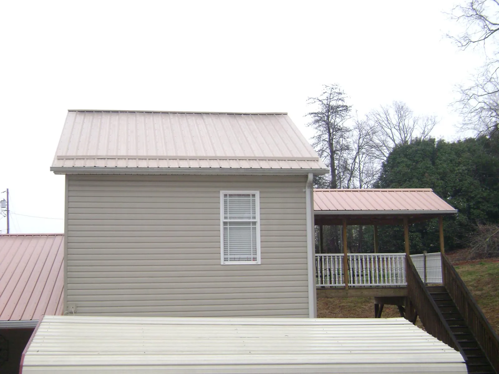Tan metal roofs on a two story addition and attached porch, from a Roof Replacement job in Prole
